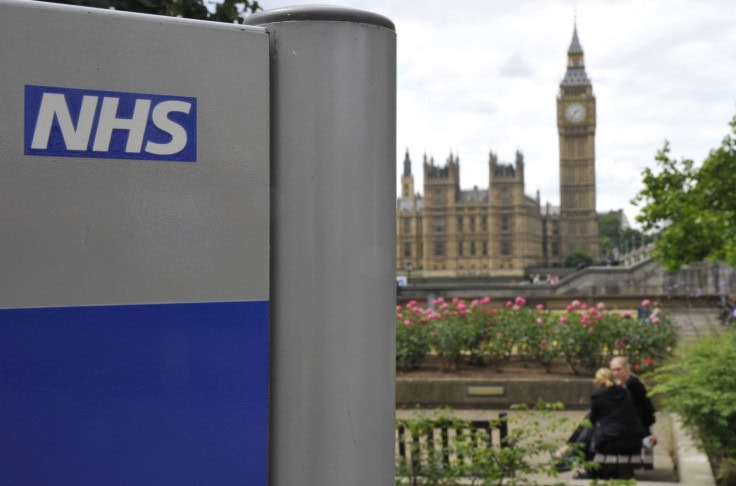 NHS health service sign with Big Ben in London, UK, in the background, during daytime.