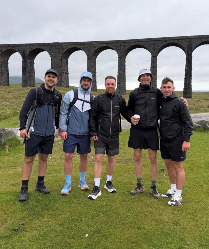 Team Melanoma UK at Yorkshire 3 Peaks Challenge with historic viaduct in background.