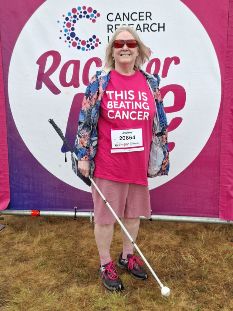 Woman with a cane at a cancer research event wearing a pink T-shirt.