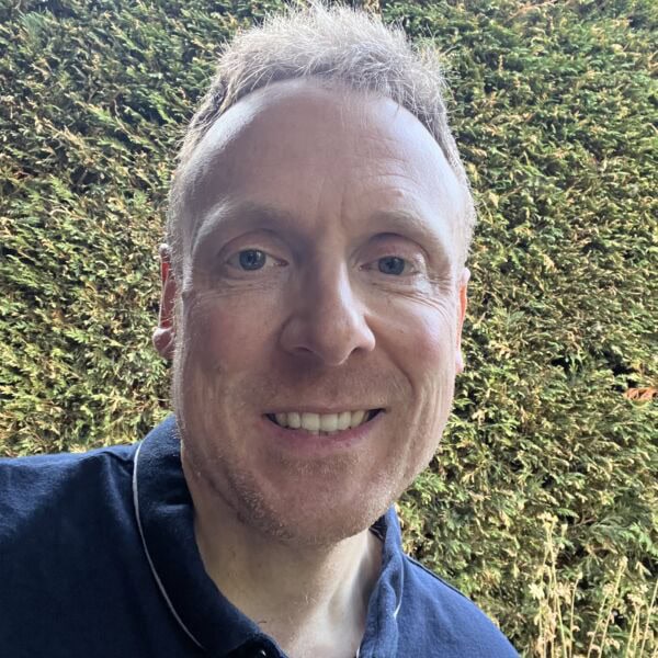 Smiling man outdoors with a hedge background, wearing a navy shirt.