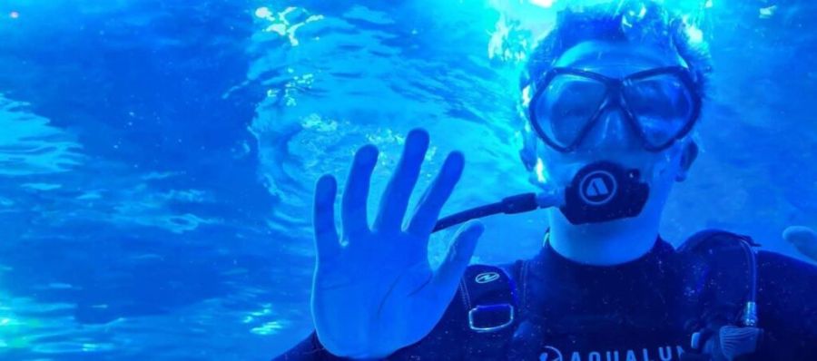 Person scuba diving underwater with mask and snorkel, raising hand.