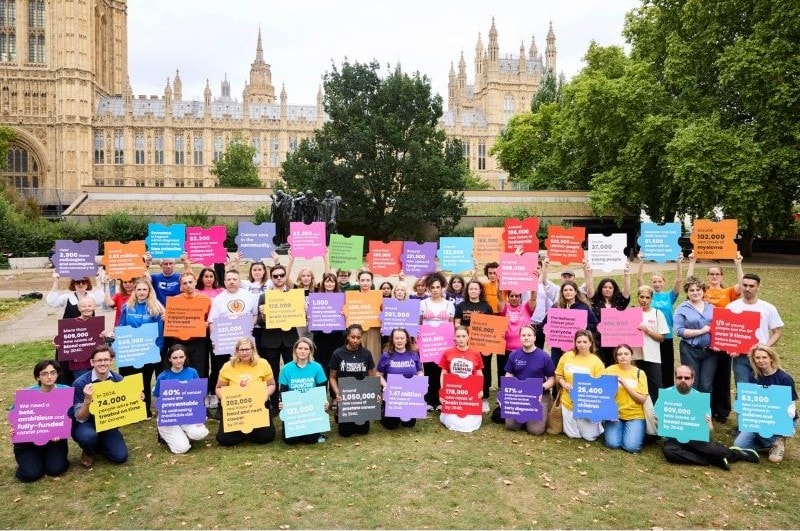 Group of people holding colourful signs in front of UK Parliament.