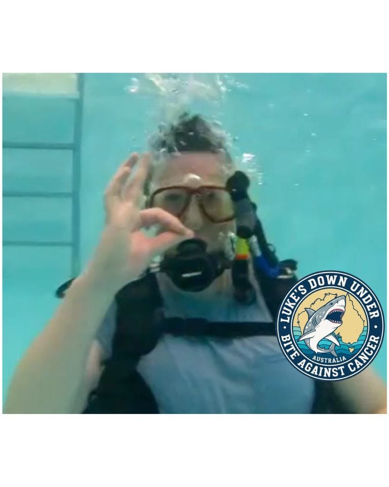 Person scuba diving underwater with a 'Lukes Down Under' shark logo.